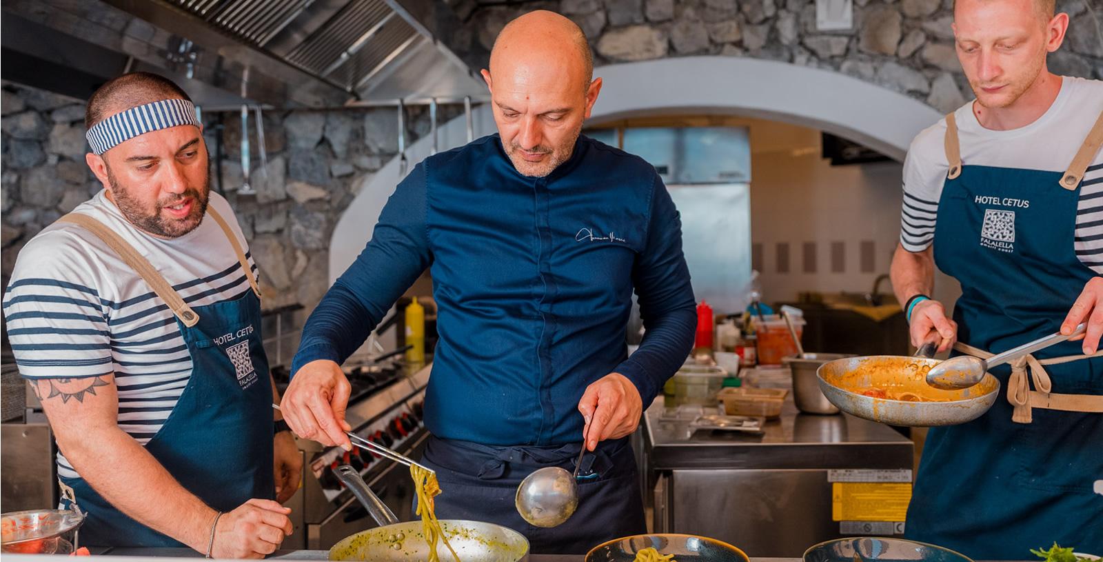 Chef cucina pasta in una cucina professionale con due assistenti.