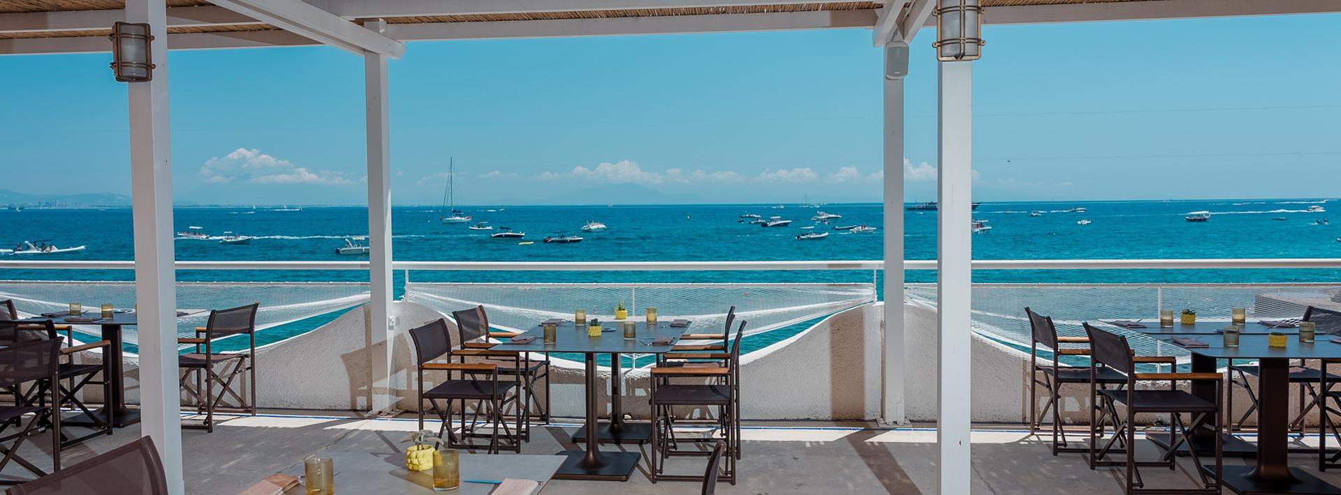 Terrazza con vista mare, tavoli apparecchiati, cielo sereno.